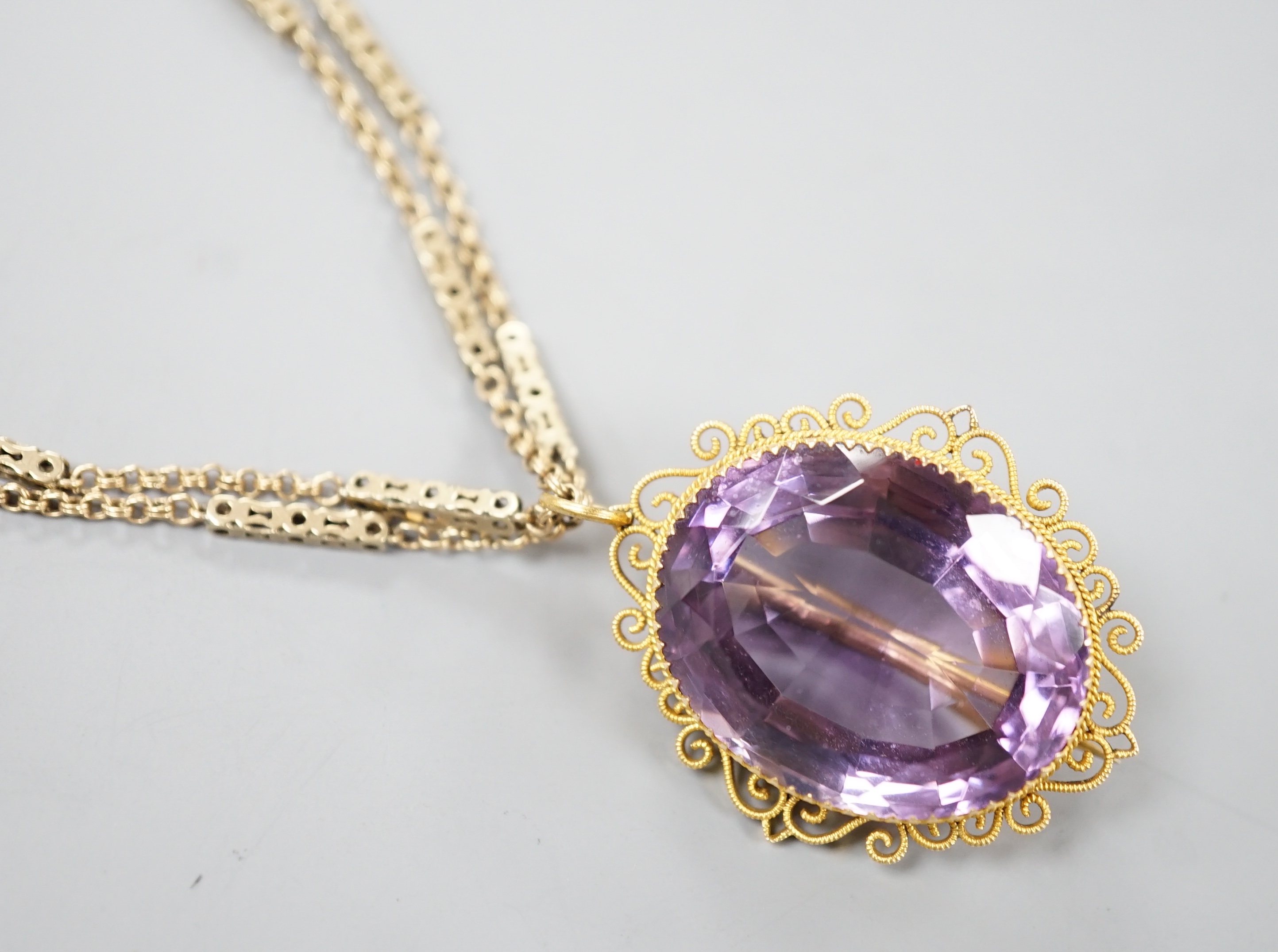 A yellow metal mounted oval cut amethyst pendant brooch, 34mm, gross 13.2 grams, on a Victorian pinchbeck guard chain, 70cm.